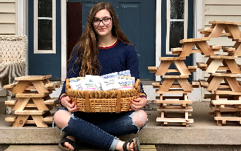 student holding basket with small picnic tables near her