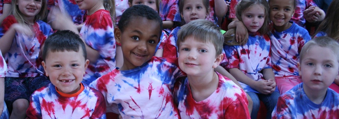 kids sitting in bleachers in red, white and blue shirts
