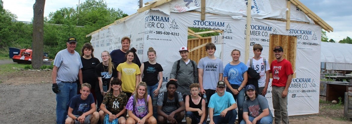 students and adults standing and kneeling in front of barn under construction