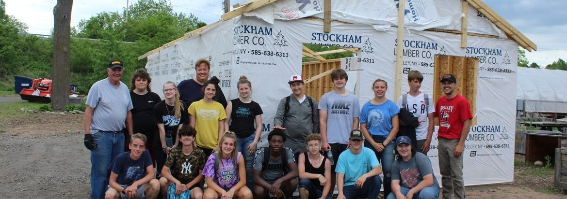 students and adults standing and kneeling in front of barn under construction