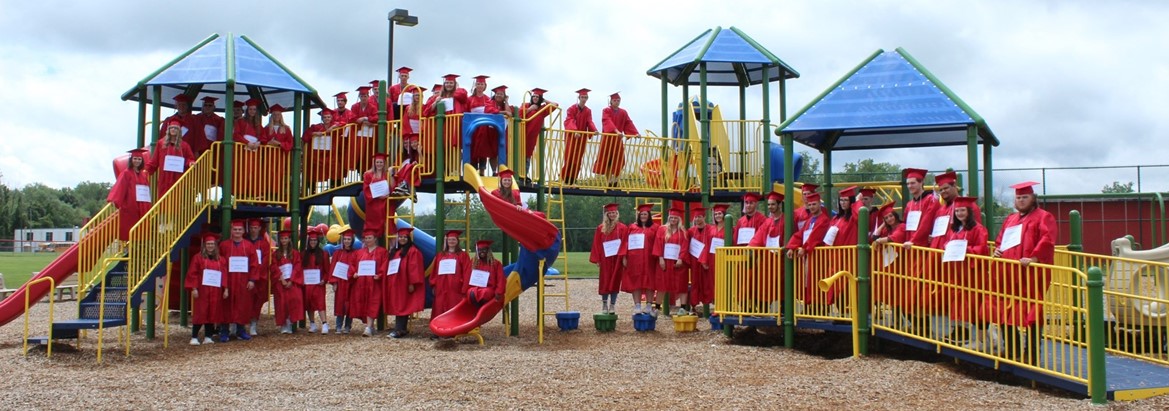 seniors standing on and near playground equipment in their caps and gowns
