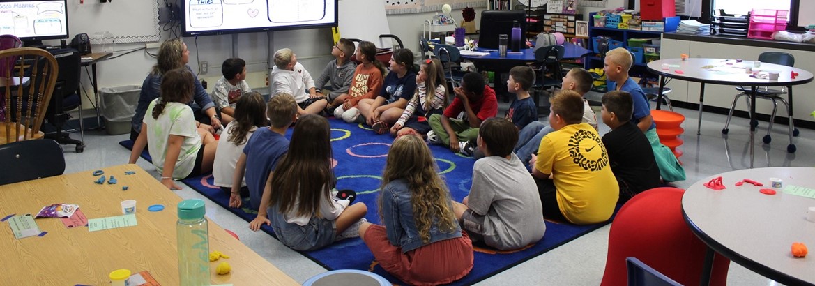 class sitting on floor in classroom looking at smartboard